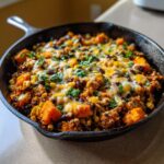 A close-up of a hearty sweet potato skillet dinner topped with melted cheese, black beans, corn, and cilantro.