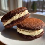 Close-up of two rich, dark chocolate tiramisu cookies filled with creamy mascarpone filling and dusted with cocoa powder.