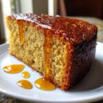 Close-up of a moist slice of Bacardi rum cake being drizzled with a thick, amber glaze.
