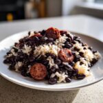 A close-up of a plate of flavorful black beans and rice mixed with slices of smoked sausage.