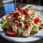 A generous serving of creamy BLT chicken salad mixed with lettuce and cherry tomatoes, piled high with crispy bacon.