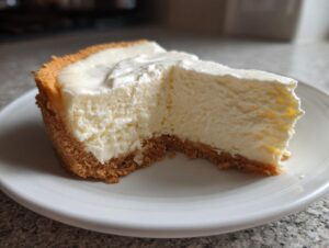 A close-up shot of a thick slice of creamy cheesecake recipe on a white plate, showing the graham cracker crust.