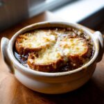 Close-up of a baked french onion soup recipe serving, topped with melted, bubbly cheese over croutons.