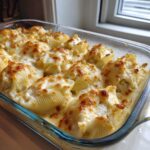 A glass baking dish filled with baked chicken alfredo stuffed shells topped with melted, bubbly, and slightly browned cheese sauce.