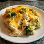 A close-up serving of creamy Chicken Divan featuring chunks of chicken, bright green broccoli florets, and a melted cheddar cheese topping.