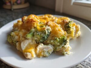 A close-up serving of creamy Chicken Divan casserole, featuring chunks of chicken, bright green broccoli florets, and melted cheddar cheese topping.
