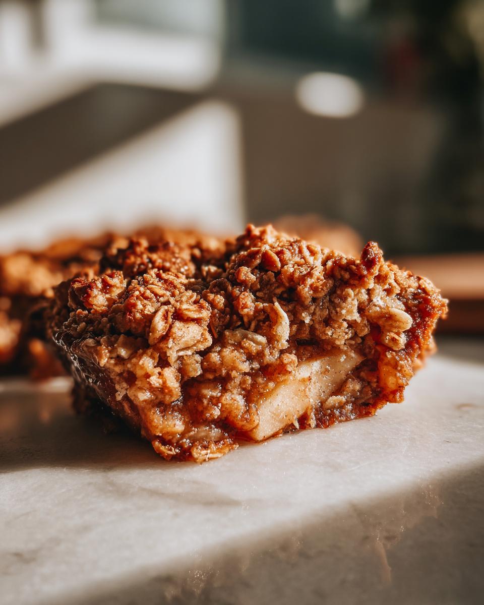 A close-up, side view of a square serving of apple crisp showing the thick, crunchy oat topping and tender apple filling.