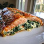A cross-section view of perfectly cooked stuffed salmon, revealing a creamy spinach filling inside the flaky fish.