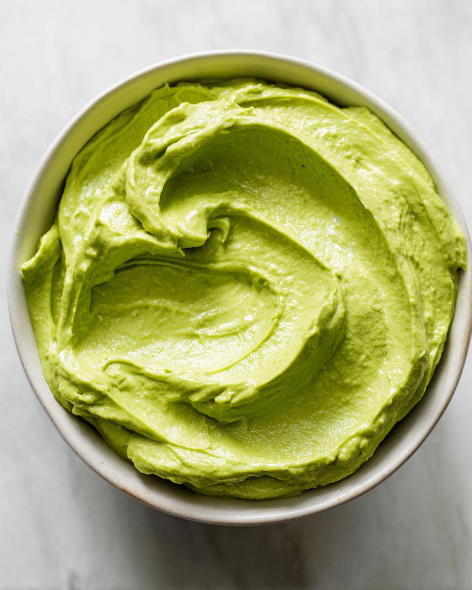 Overhead close-up of a bowl filled with smooth, bright green avocado sauce, showing creamy swirls.