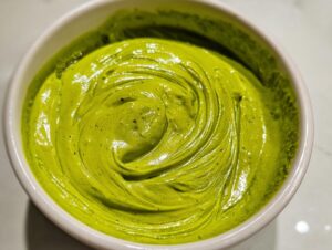 Close-up overhead shot of thick, vibrant green avocado sauce swirled in a small white bowl.