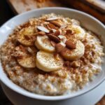 Close-up of creamy banana oatmeal topped with sliced bananas, slivered almonds, and a generous dusting of cinnamon.