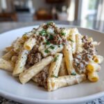 A close-up of a plate piled high with creamy beef pasta (rigatoni style) topped with ground beef and fresh parsley.