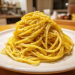 A tall mound of creamy lemon pasta tossed in a rich yellow sauce and topped with fresh black pepper.