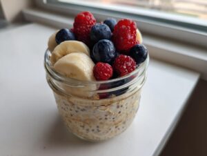 A jar of creamy overnight oats topped generously with fresh raspberries, blueberries, and sliced bananas.
