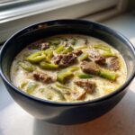 Close-up of creamy philly cheese steak soup featuring slices of beef and bright green bell peppers in a dark bowl.