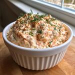 A white bowl filled with creamy smoked salmon dip, garnished generously with fresh dill and cracked pepper.