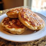 Close-up of three perfectly golden-brown, fluffy banana pancakes stacked on a white plate.