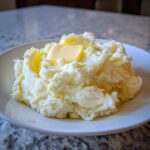 A generous serving of creamy, fluffy mashed potatoes topped with a melting pat of butter.