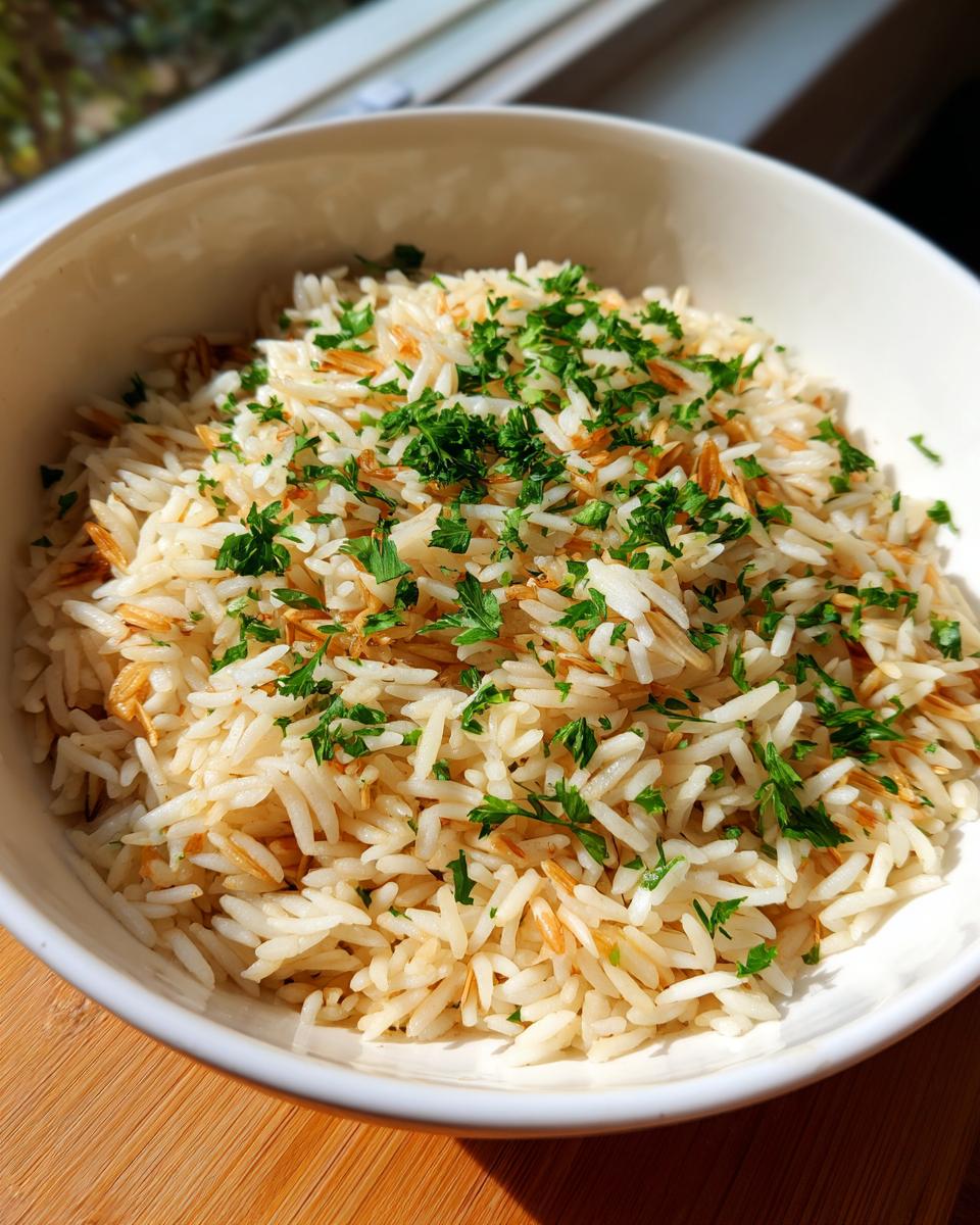 A white bowl filled with fluffy rice pilaf mixed with toasted vermicelli and garnished with chopped green parsley.