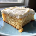 A thick, square slice of soft sugar cookie bars topped with creamy white frosting, resting on a blue plate.