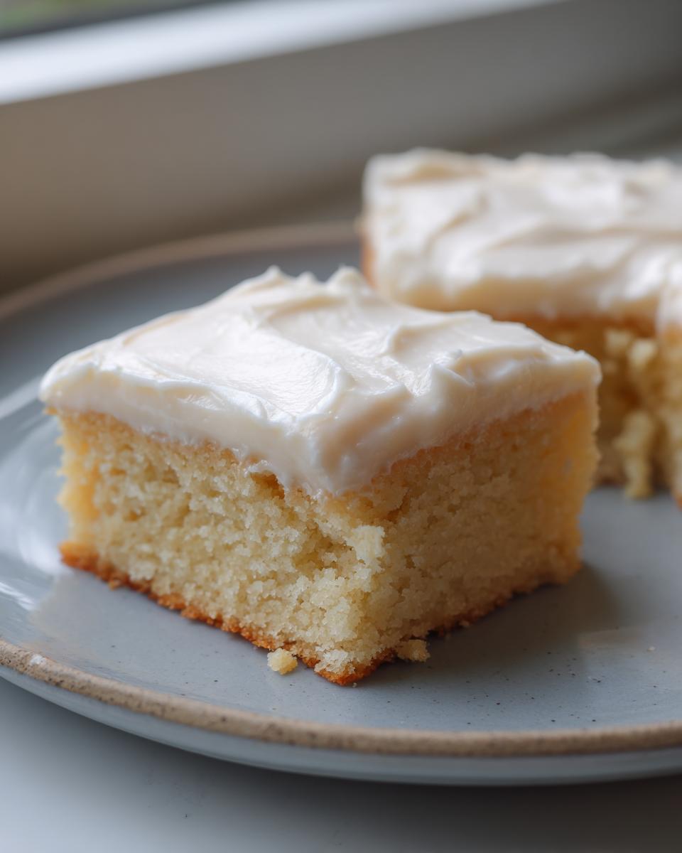 Close-up of a square slice of soft sugar cookie bars topped with thick white frosting.
