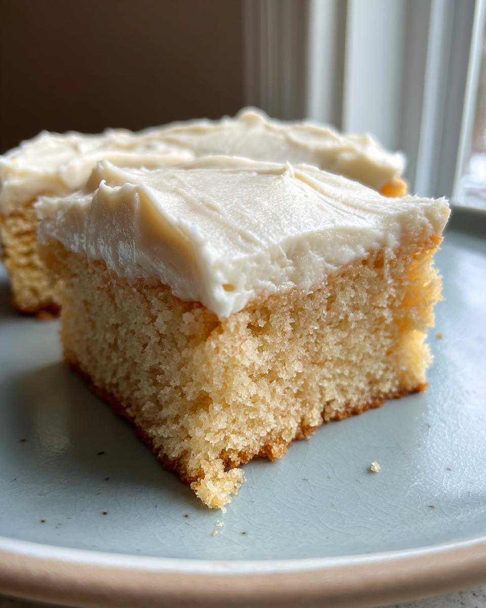A close-up of a square slice of soft, light-colored sugar cookie bars topped with thick white frosting.