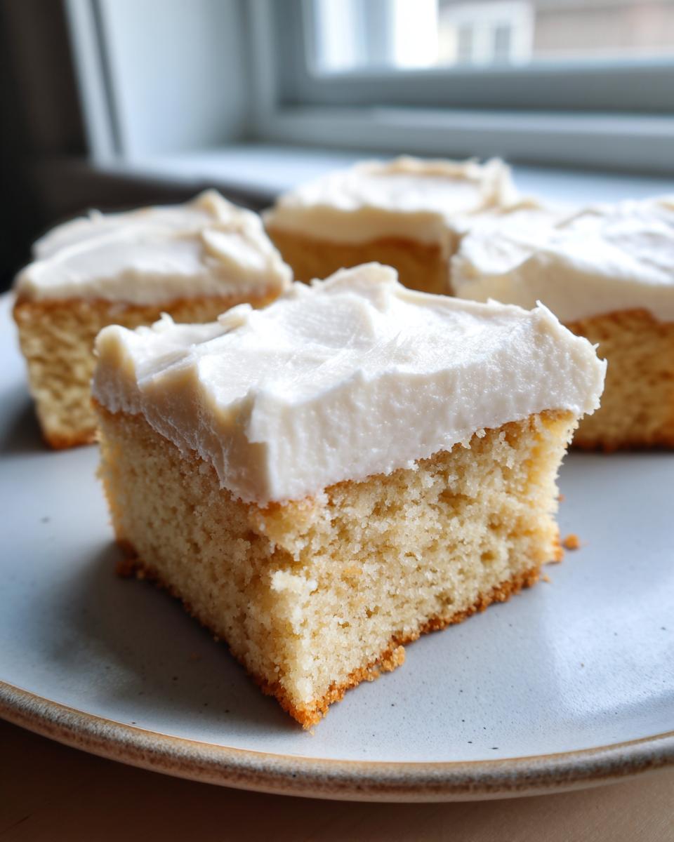 A close-up shot of a thick, square slice of soft sugar cookie bars topped with creamy white frosting.