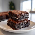 Two fudgy oreo brownies stacked on a white plate, showing the creamy white filling inside the dark chocolate.