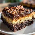 Close-up of a rich slice of german chocolate cheesecake showing chocolate crust, creamy layer, and pecan topping.