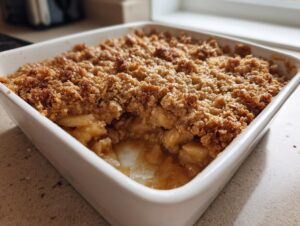 Close-up of a freshly baked apple crisp recipe with a thick, golden brown, crumbly topping in a white square baking dish.