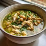 Close-up of a bowl of green chicken pozole featuring shredded chicken, hominy, and fresh cilantro garnish.
