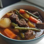 Close-up of a hearty bowl of vegetable beef soup featuring chunks of beef, potatoes, carrots, and green beans in a rich broth.
