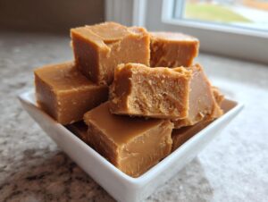 Close-up of several rich, brown sugar penuche fudge squares stacked in a small white dish.
