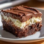 Close-up of a moist slice of Italian love cake showing a dark chocolate base, creamy white layer, and thick chocolate frosting.