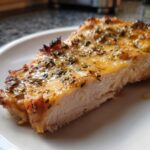 Close-up of a juicy baked chicken breast slice showing moist white meat and a golden, herbed topping.