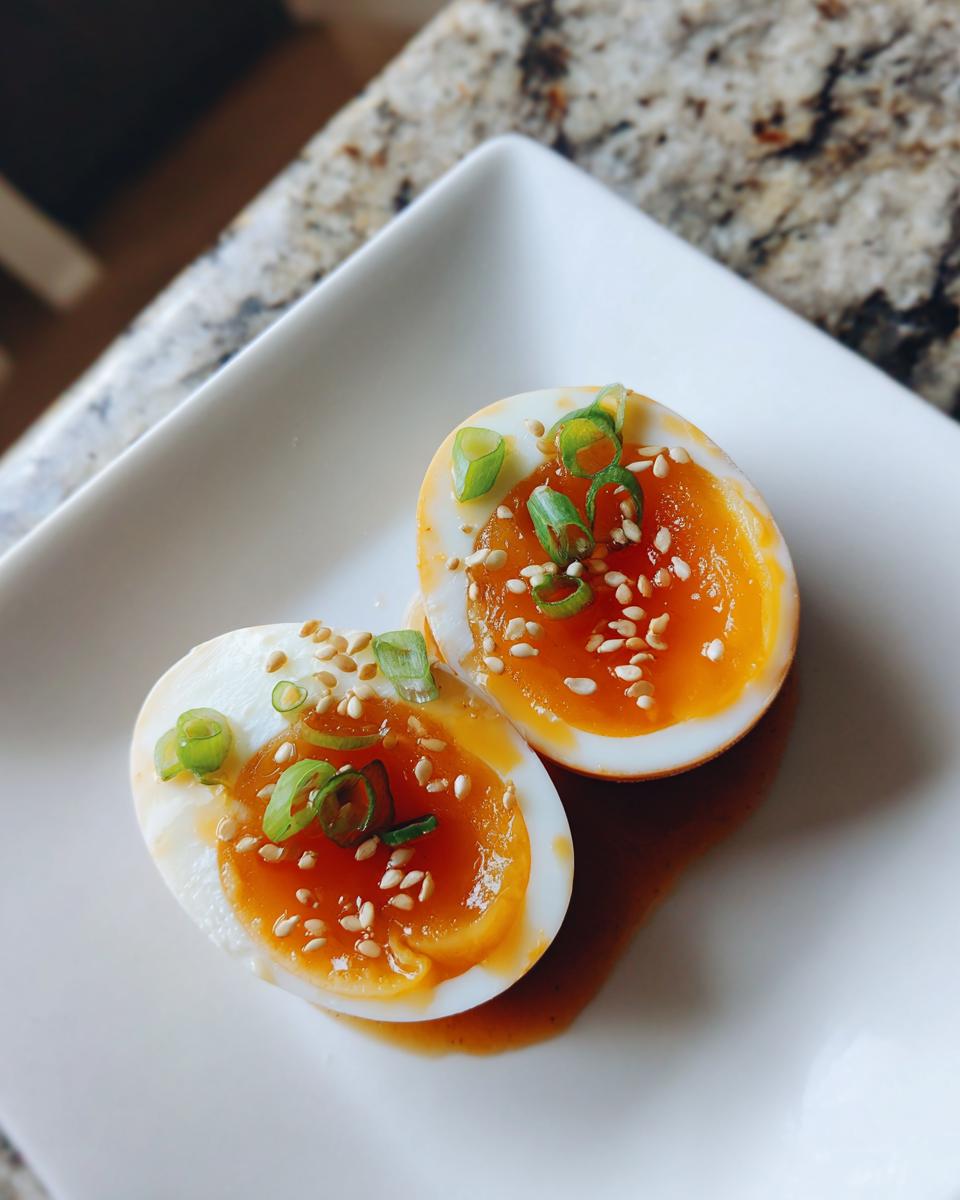 Two halves of soft-boiled marinated eggs with jammy yolks, topped with sesame seeds and green onions.