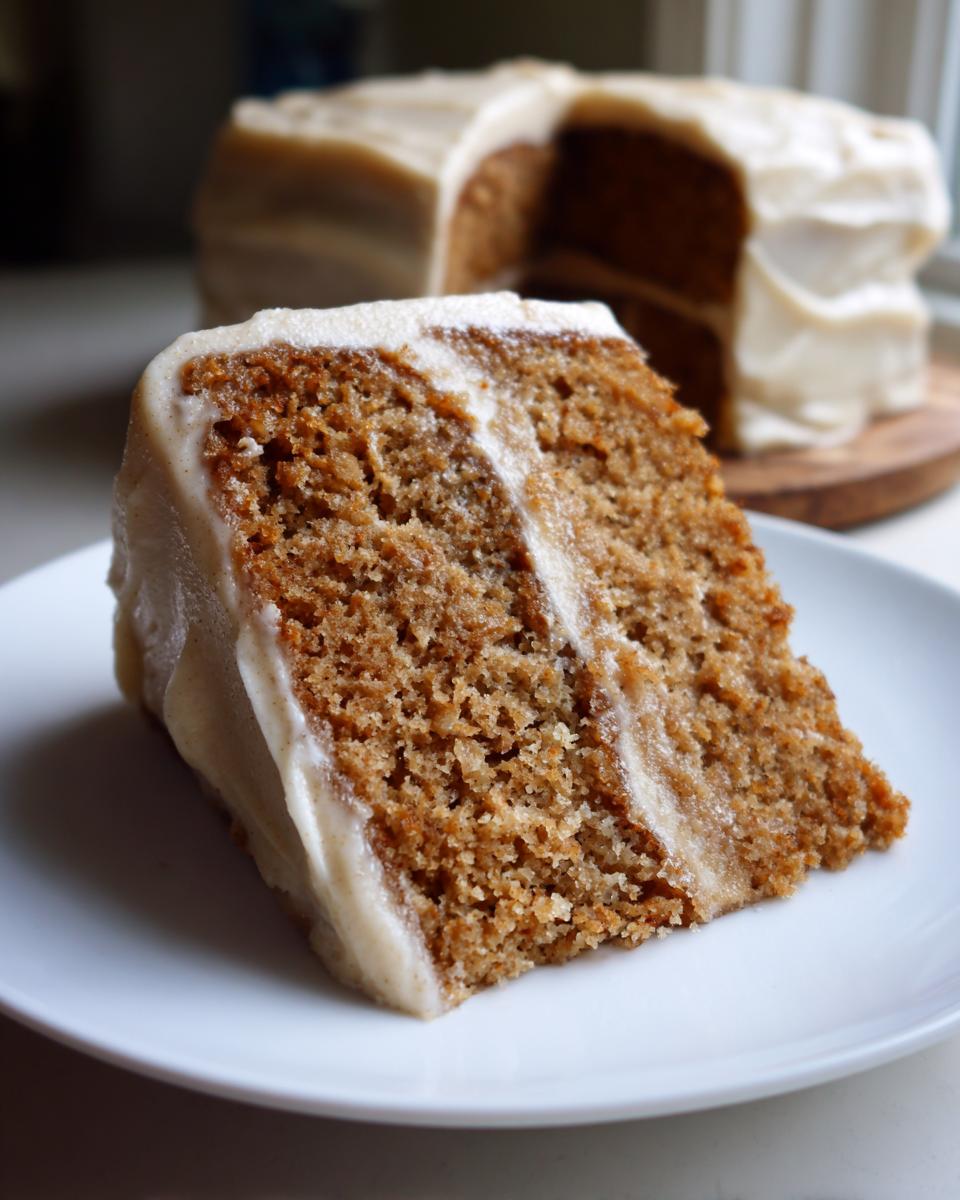 Close-up of a thick slice of moist applesauce cake layered with creamy frosting on a white plate.