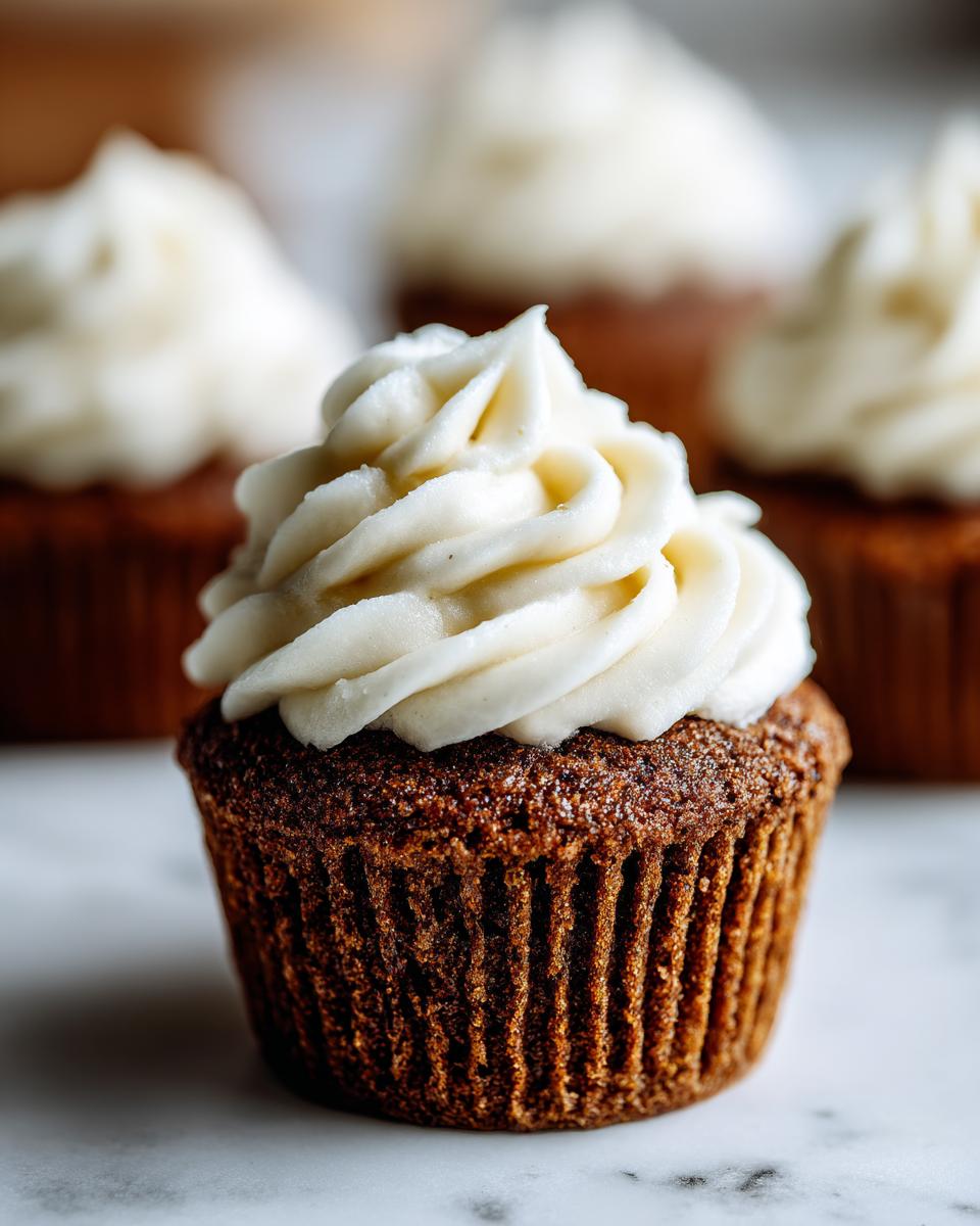 Close-up of a single, moist gingerbread cupcakes topped with a swirl of white cream cheese frosting.
