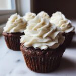 Close-up of moist gingerbread cupcakes topped with a swirl of white cream cheese frosting.