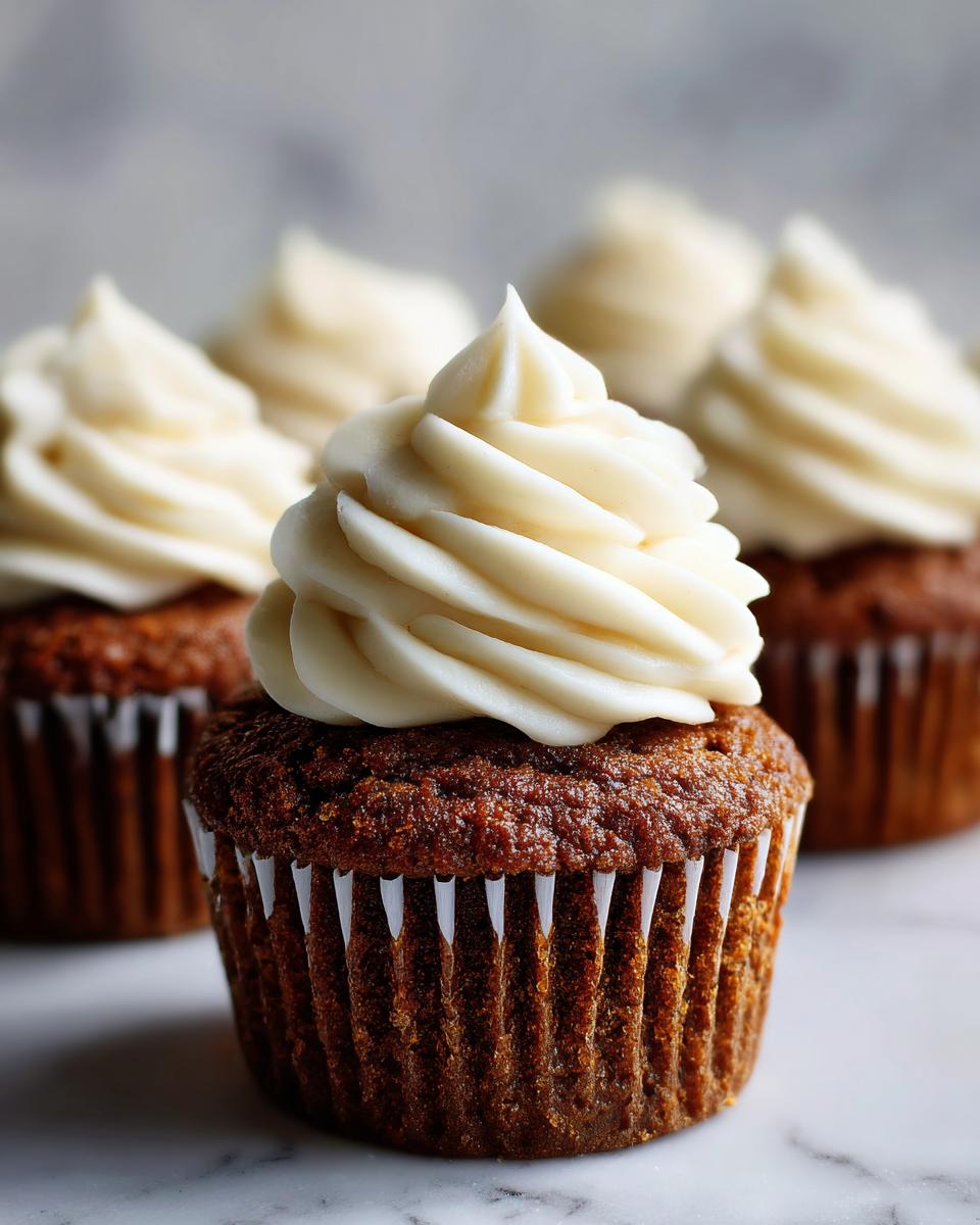 Close-up of a perfectly frosted gingerbread cupcake with rich brown cake and white swirl frosting.