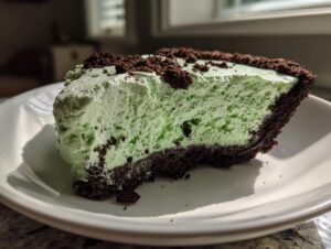 A close-up of a thick slice of light green, fluffy no-bake grasshopper pie with a dark chocolate crust.