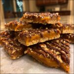 A stack of homemade Pecan Pie Bark bars featuring a thick caramel layer, pecans, and a dark chocolate drizzle on a marble surface.