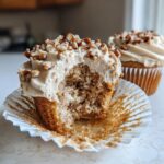 Close-up of a pecan pie cupcakes with a bite taken out, showing the moist crumb and pecan-topped frosting.