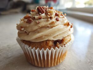 A single, delicious pecan pie cupcake topped with thick, light brown frosting and chopped pecans.