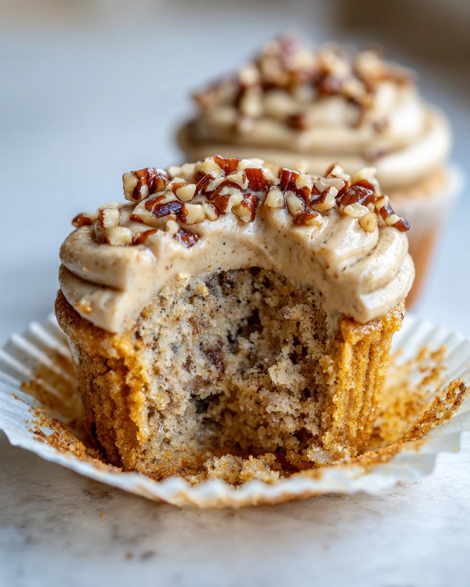 Close-up of a pecan pie cupcakes cut in half showing the moist interior and brown sugar frosting topped with chopped pecans.