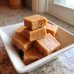 A stack of perfectly cut, light brown squares of creamy penuche fudge served in a small white dish.