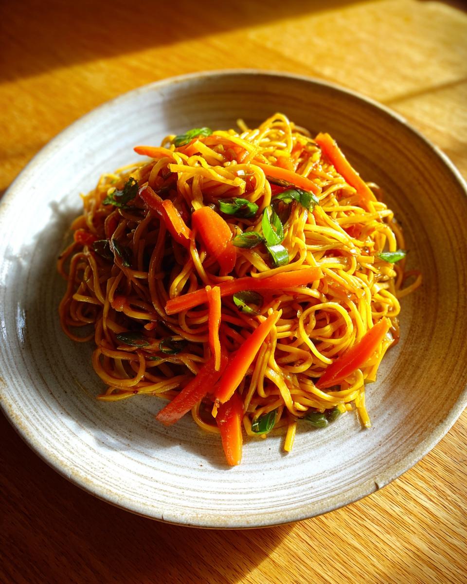 A serving of vibrant, golden fried noodles mixed with bright orange julienned carrots and green onions.