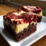 Two rich squares of red velvet cheesecake brownies showing a dark brownie base and a swirled red and cream cheese topping.