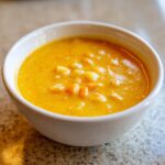 Close-up of a creamy, vibrant orange cheese soup with visible chunks of potato or vegetable.