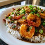 Close-up of a hearty bowl of shrimp etouffee served over white rice and topped with fresh green onions.